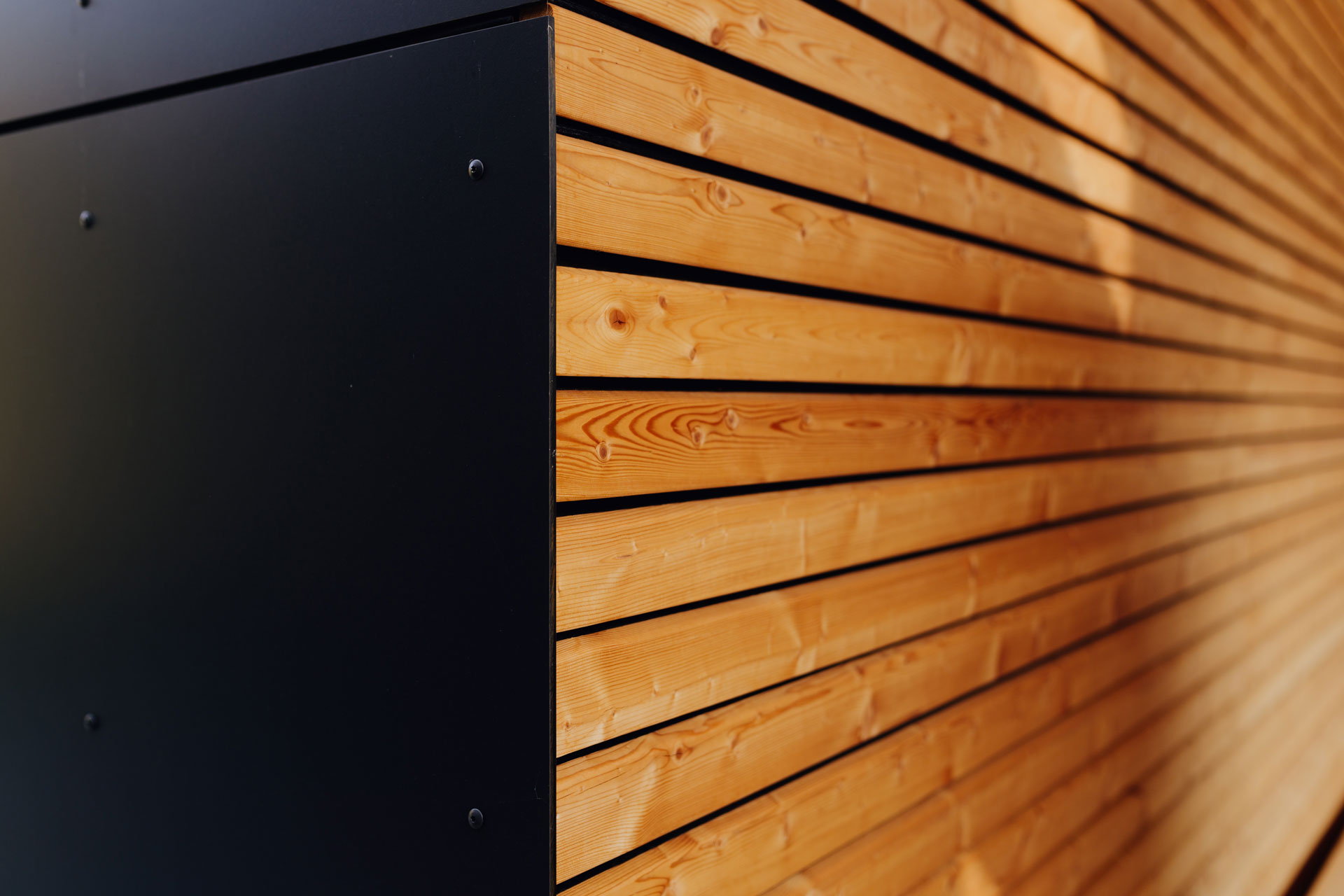Hellbraunes Holz eines Carports grenzt an schiefergraue Außenverkleidung an. Es ist eine Detailaufnahme.